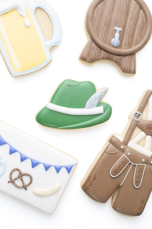 Oktoberfest themed cookies. An alpine hat decorated sugar cookie next to a beer keg, beer mug, and lederhosen decorated sugar cookies.
