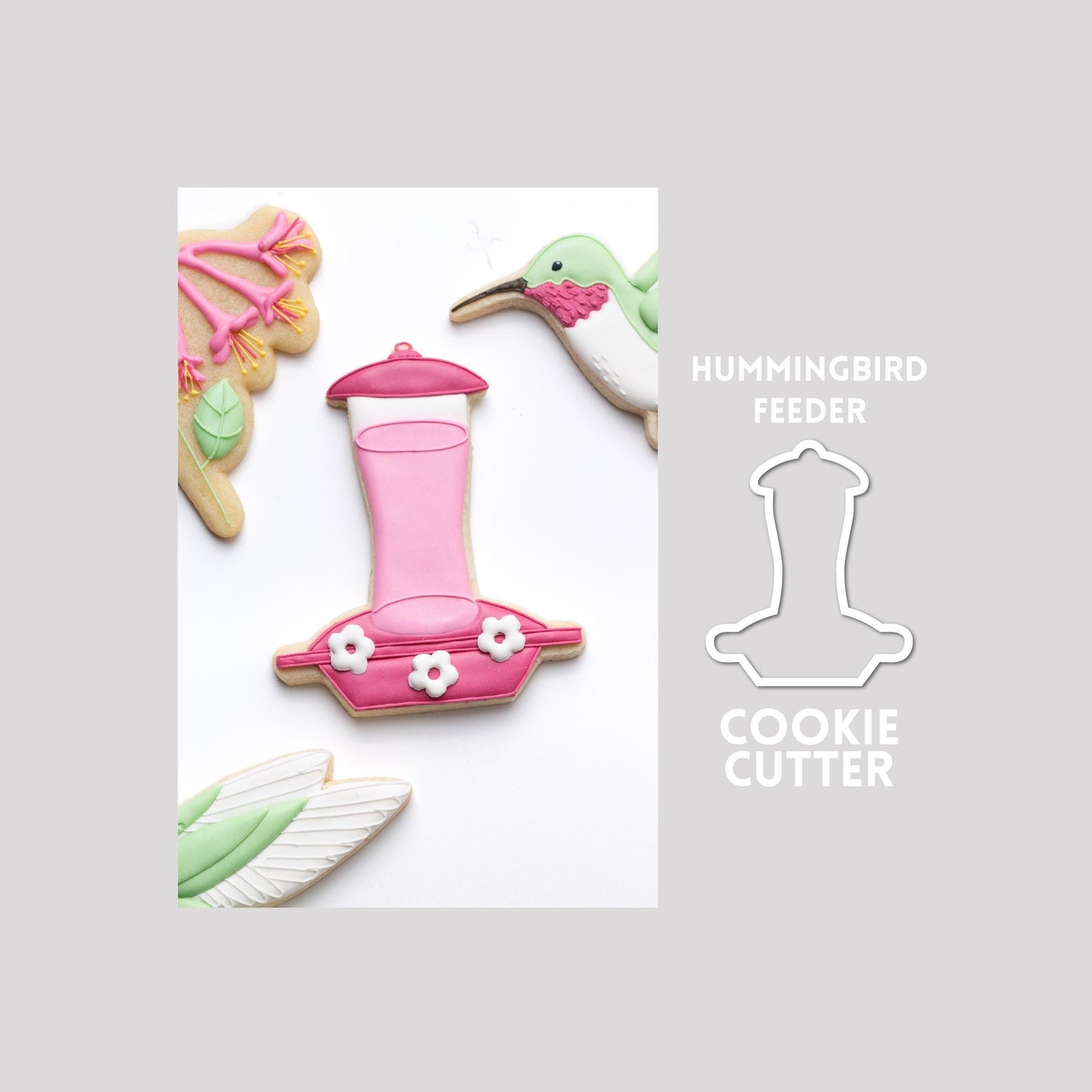Decorated hummingbird feeder sugar cookie next to a hummingbird feeder cookie cutter outline on a gray background.