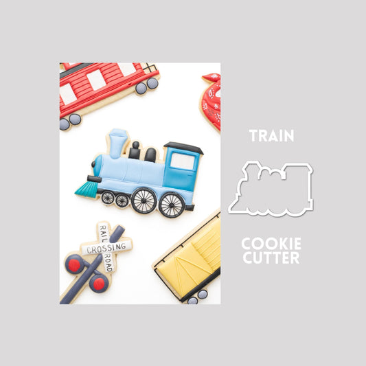 Decorated train sugar cookie next to a train cookie cutter outline on a gray background.