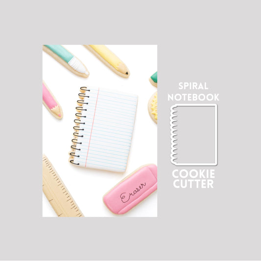 Decorated spiral notebook sugar cookie next to a spiral notebook cookie cutter outline on a gray background.
