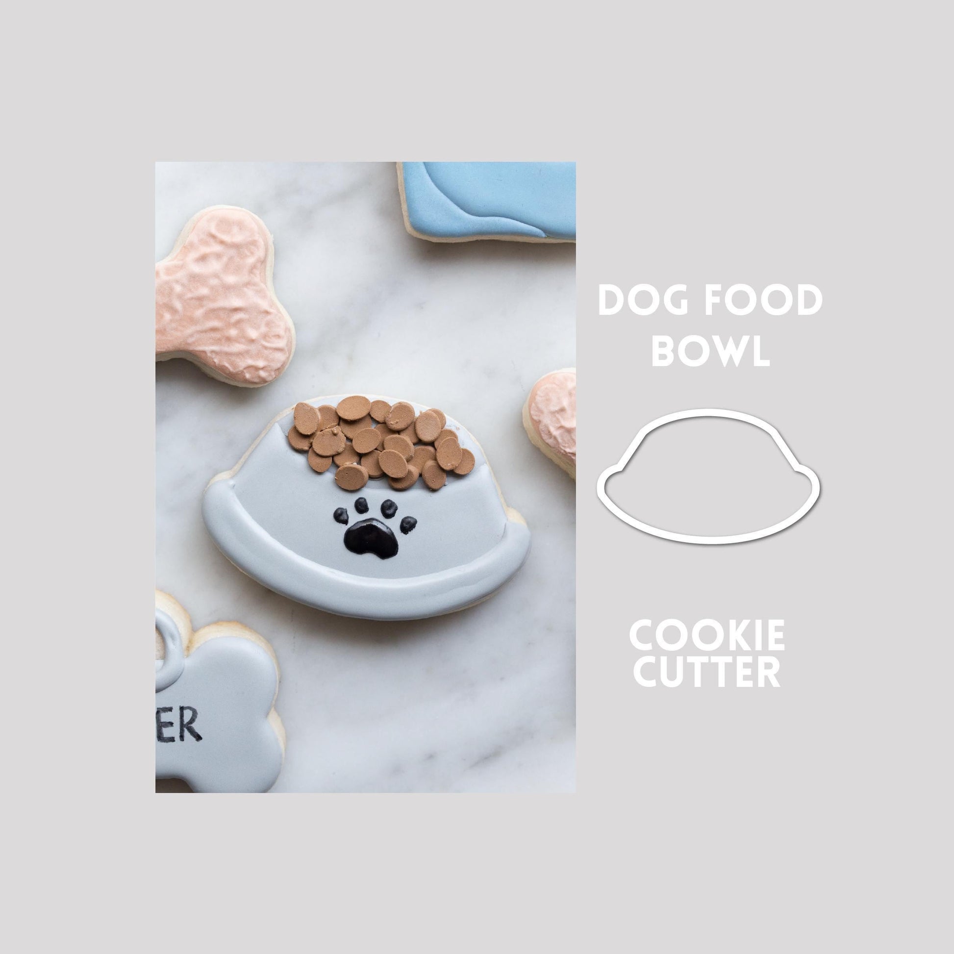Decorated dog food bowl sugar cookie next to a dog food bowl cookie cutter outline on a gray background.