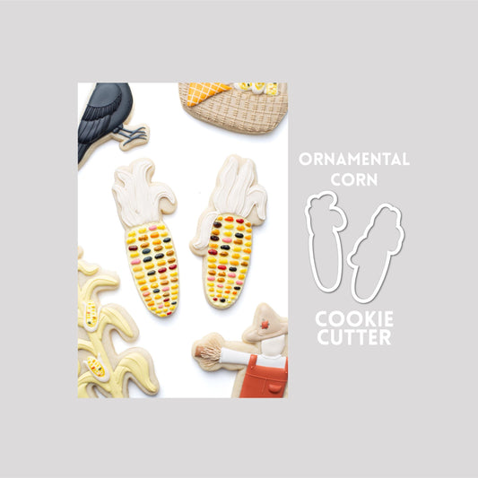 Decorated ornamental corn sugar cookie next to a ornamental corn cookie cutter outline on a gray background.