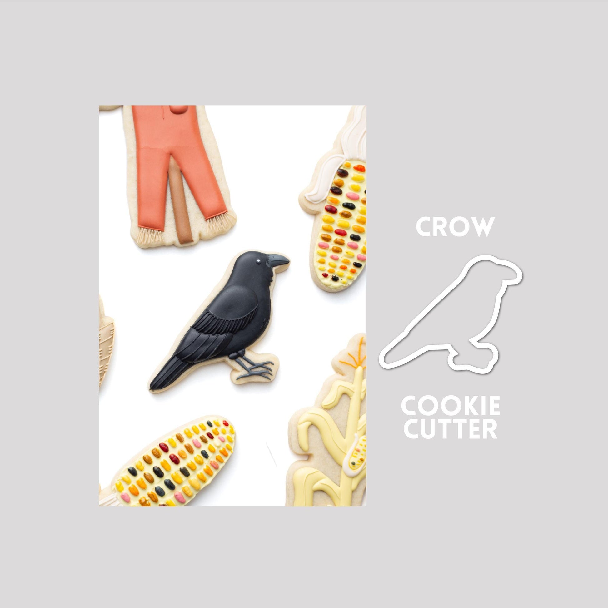 Decorated crow sugar cookie next to a crow cookie cutter outline on a gray background.