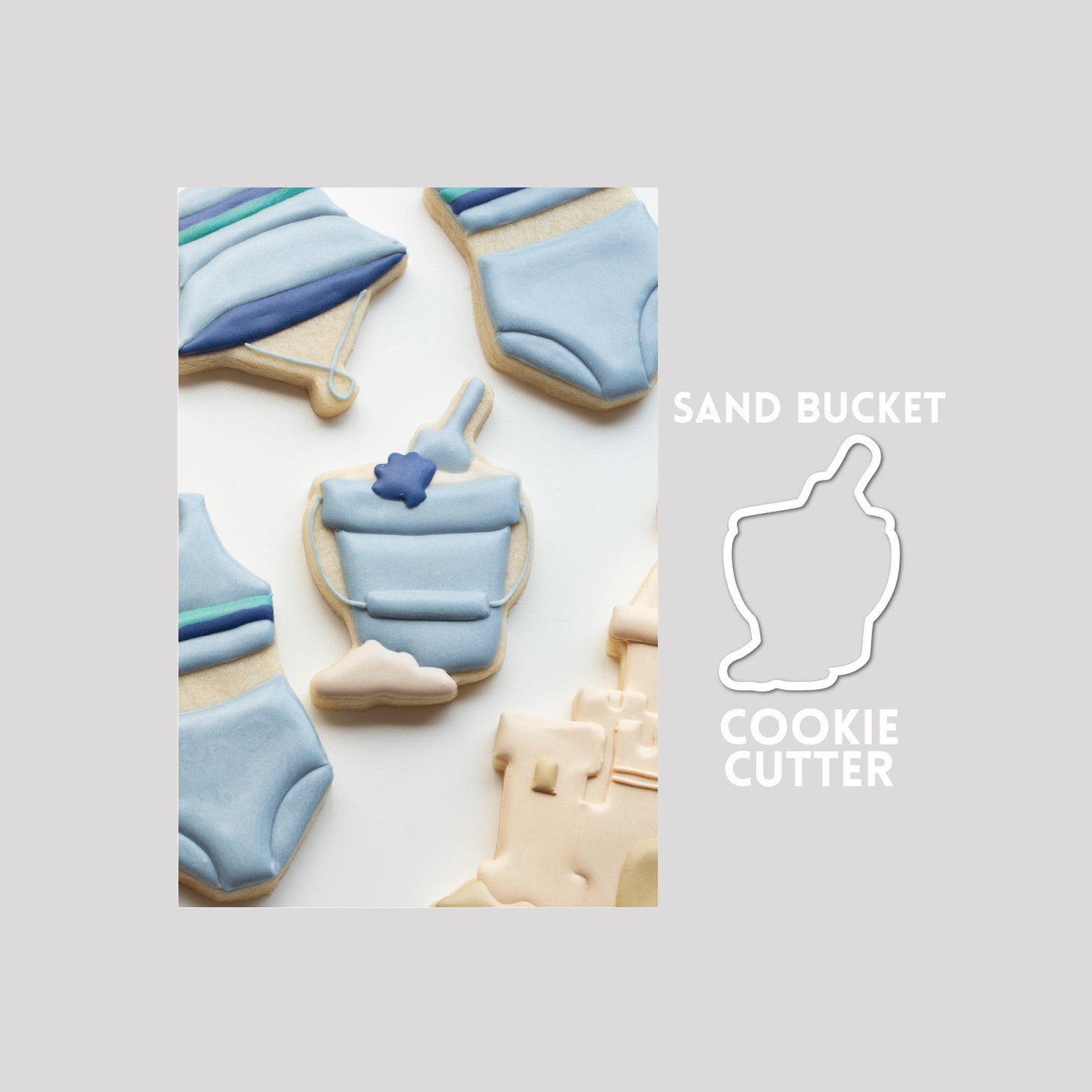 Decorated sand bucket sugar cookie next to a sand bucket cookie cutter outline on a gray background.