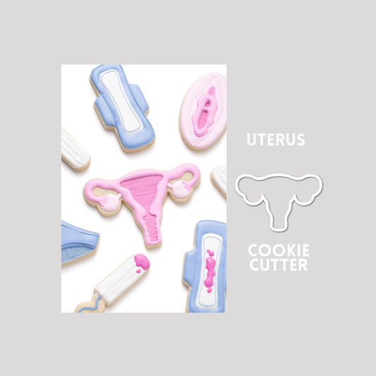 Decorated uterus sugar cookie next to a uterus cookie cutter outline on a gray background.