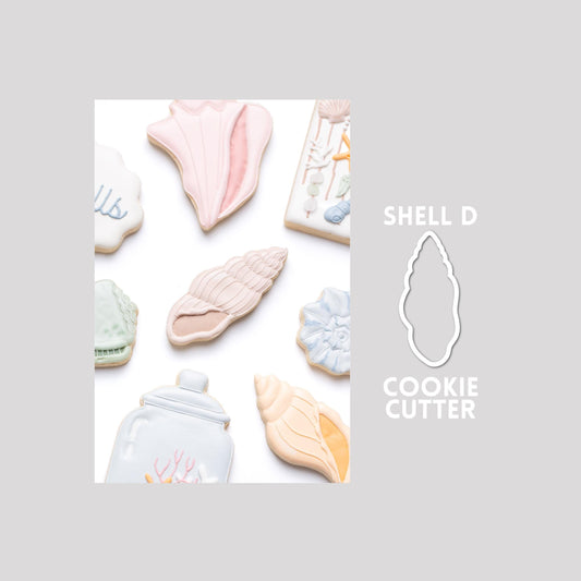 Decorated seashell sugar cookie next to a seashell cookie cutter outline on a gray background.