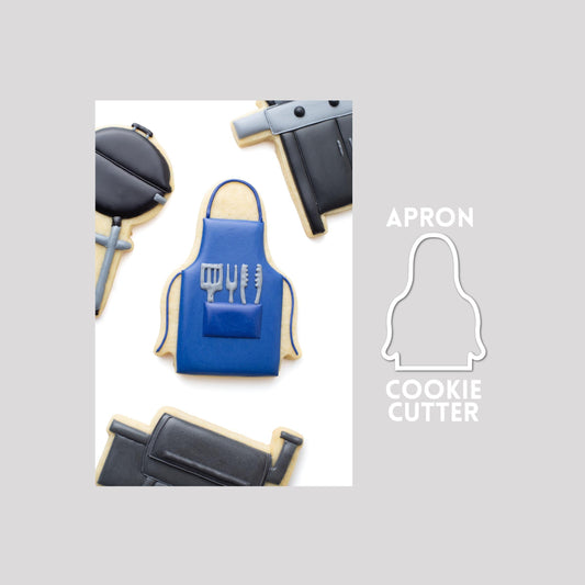 Decorated apron sugar cookie next to a apron cookie cutter outline on a gray background.