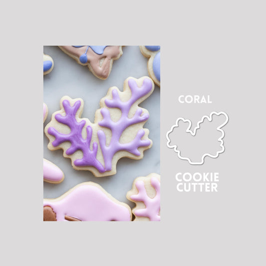 Decorated coral sugar cookie next to a coral cookie cutter outline on a gray background.
