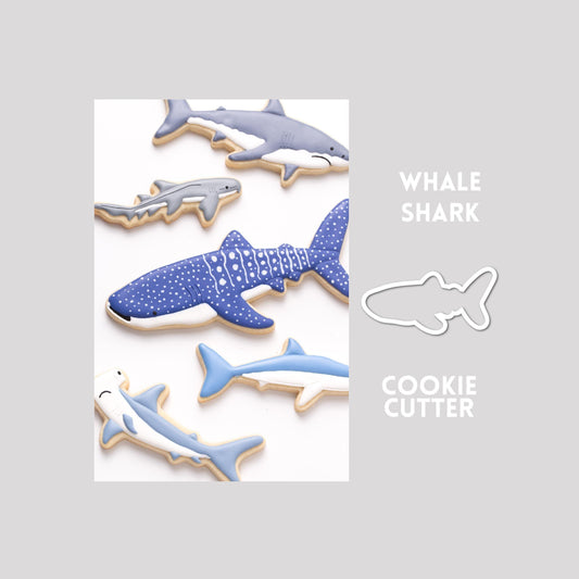 Decorated whale shark sugar cookie next to a whale shark cookie cutter outline on a gray background.