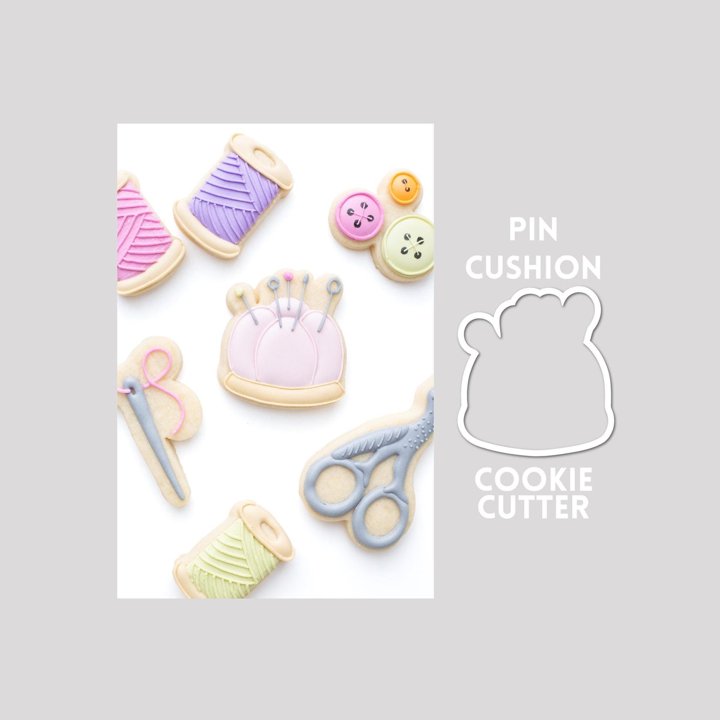 Decorated pin cushion sugar cookie next to a pin cushion cookie cutter outline on a gray background.