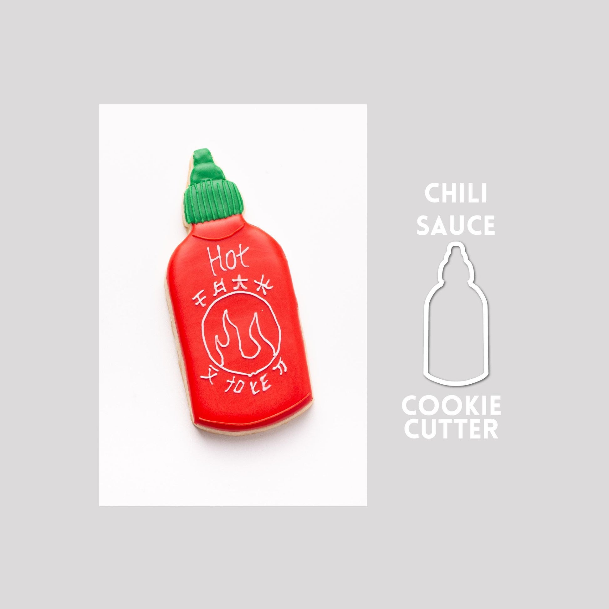 Decorated chili sauce sugar cookie next to a chili sauce cookie cutter outline on a gray background.