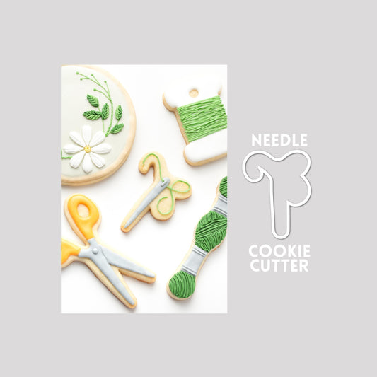 Decorated sewing needle sugar cookie next to a sewing needle cookie cutter outline on a gray background.