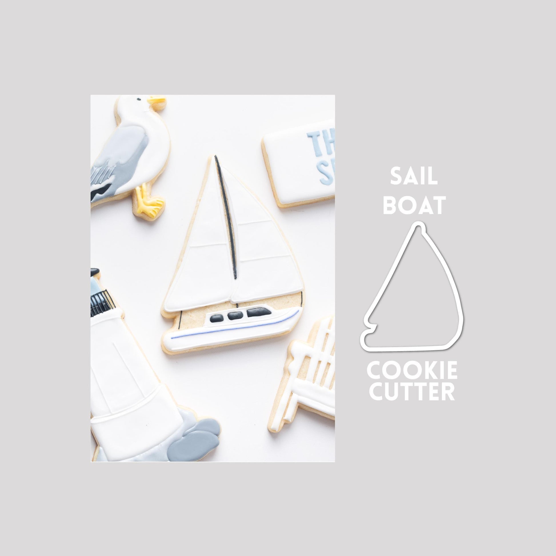 Decorated sailboat sugar cookie next to a sailboat cookie cutter outline on a gray background.