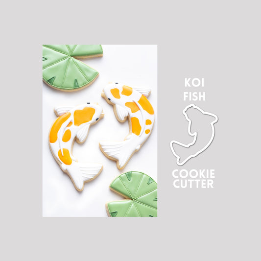 Decorated koi fish sugar cookie next to a koi fish cookie cutter outline on a gray background.