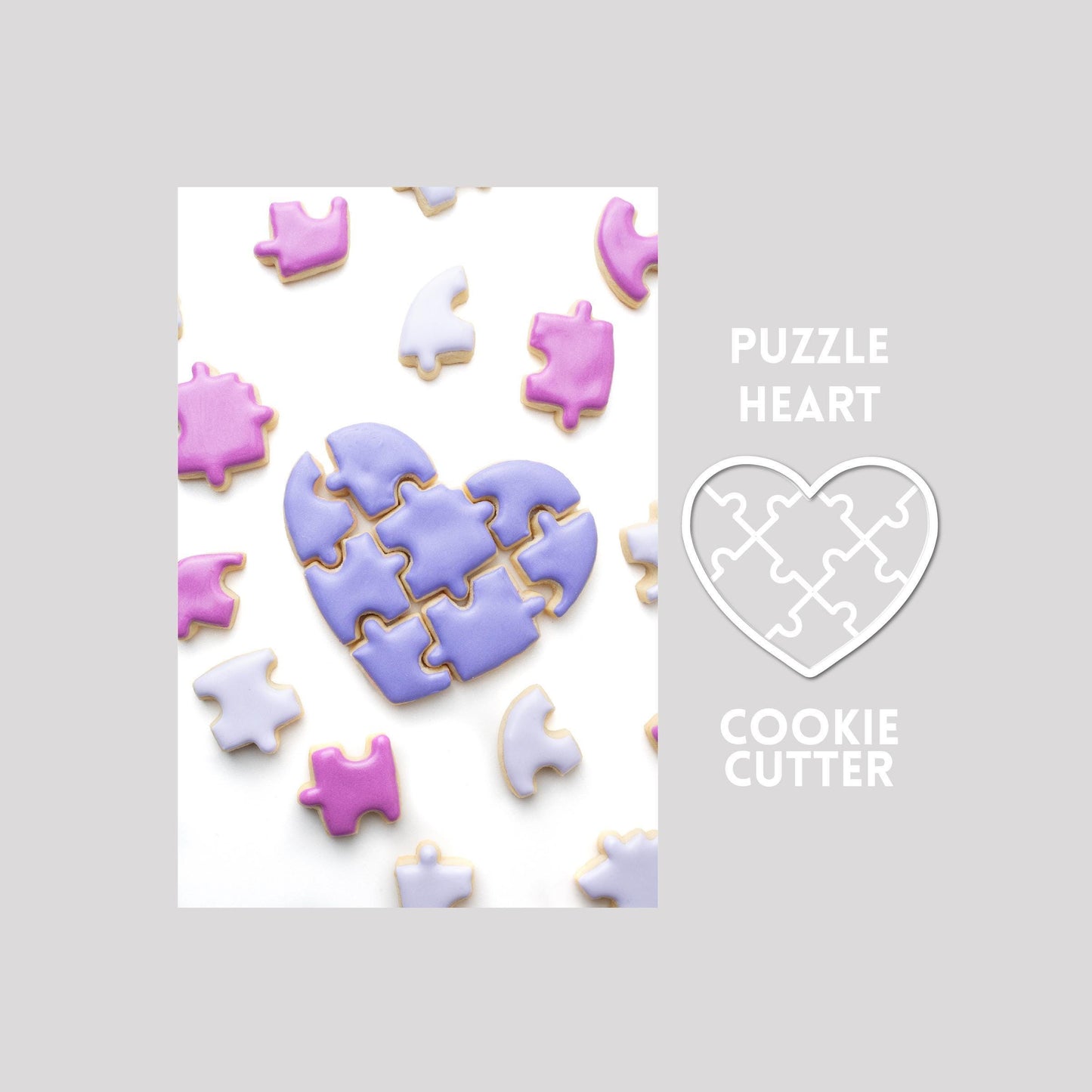 Decorated puzzle heart sugar cookie with puzzle pieces next to a puzzle heart cookie cutter outline on a gray background.