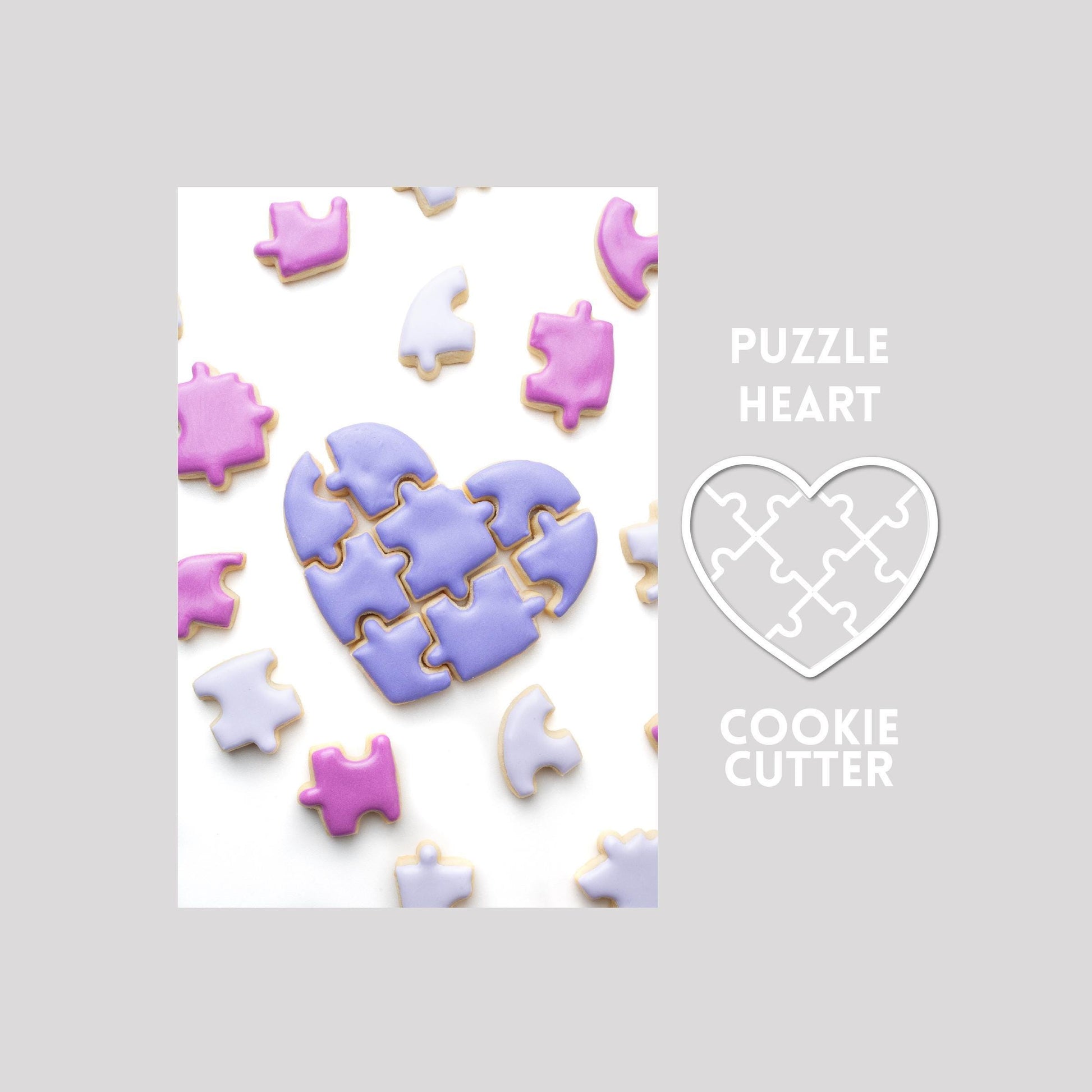 Decorated puzzle heart sugar cookie with puzzle pieces next to a puzzle heart cookie cutter outline on a gray background.