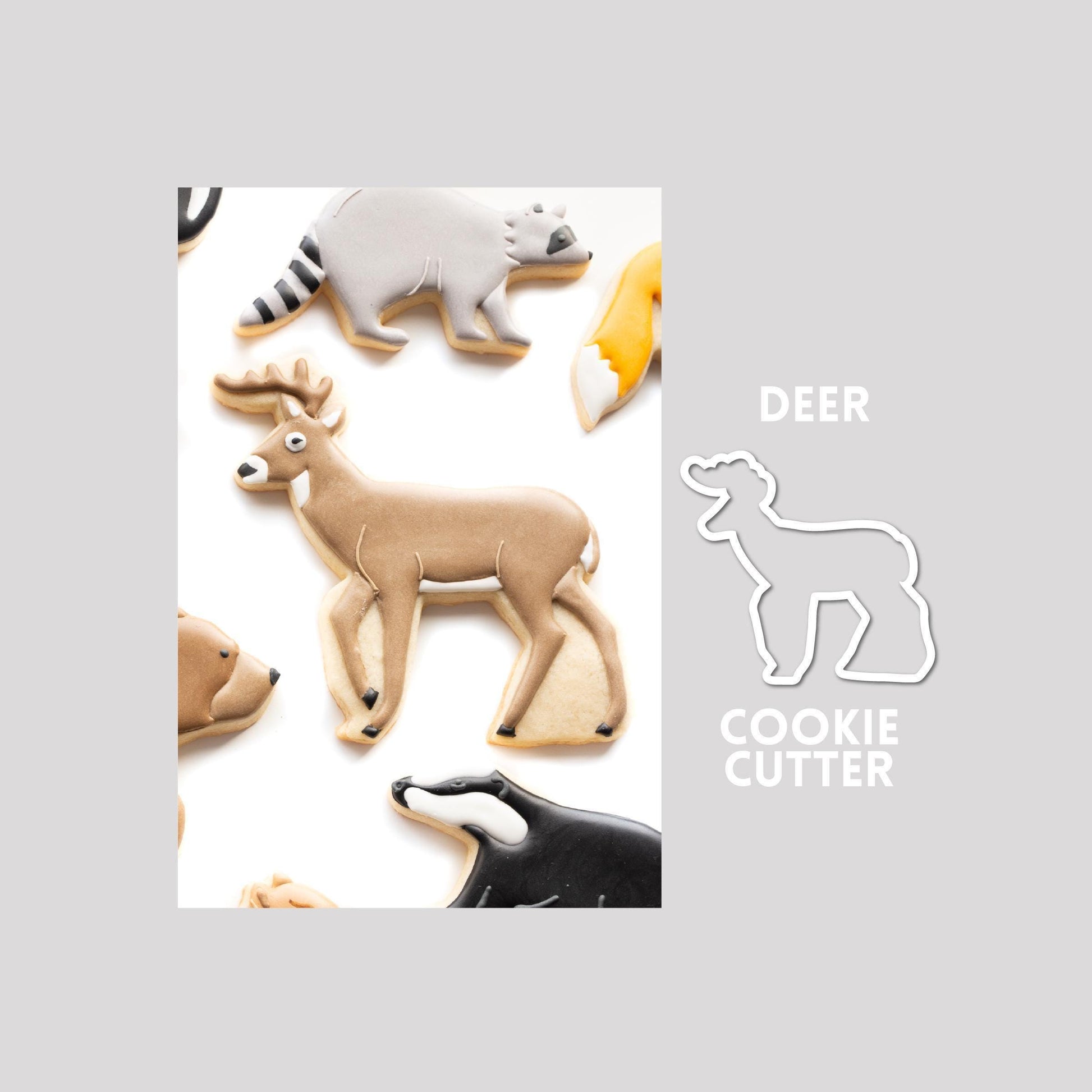 Decorated deer sugar cookie next to a deer cookie cutter outline on a gray background.