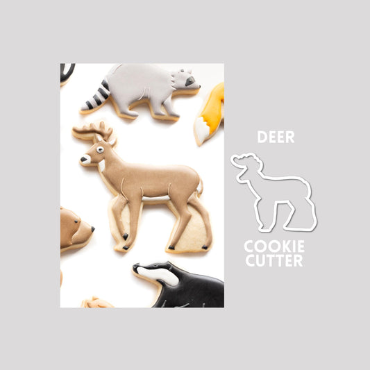 Decorated deer sugar cookie next to a deer cookie cutter outline on a gray background.