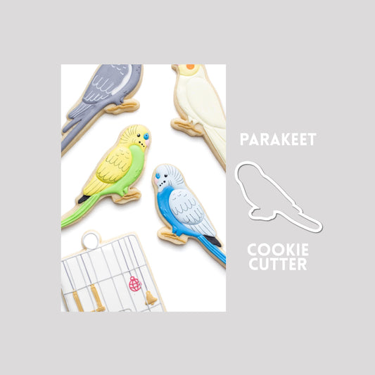 Decorated Parakeet sugar cookie next to a Parakeet cookie cutter outline on a gray background.