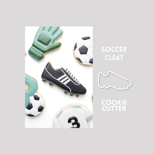 Decorated soccer cleat sugar cookie next to a soccer cleat cookie cutter outline on a gray background.