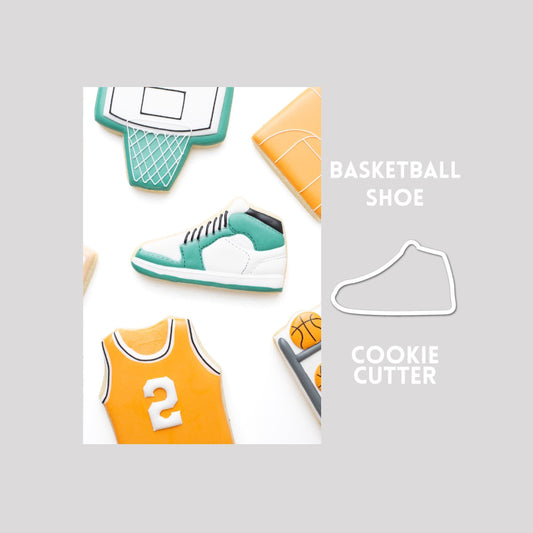 Decorated basketball shoe sugar cookie next to a basketball shoe cookie cutter outline on a gray background.