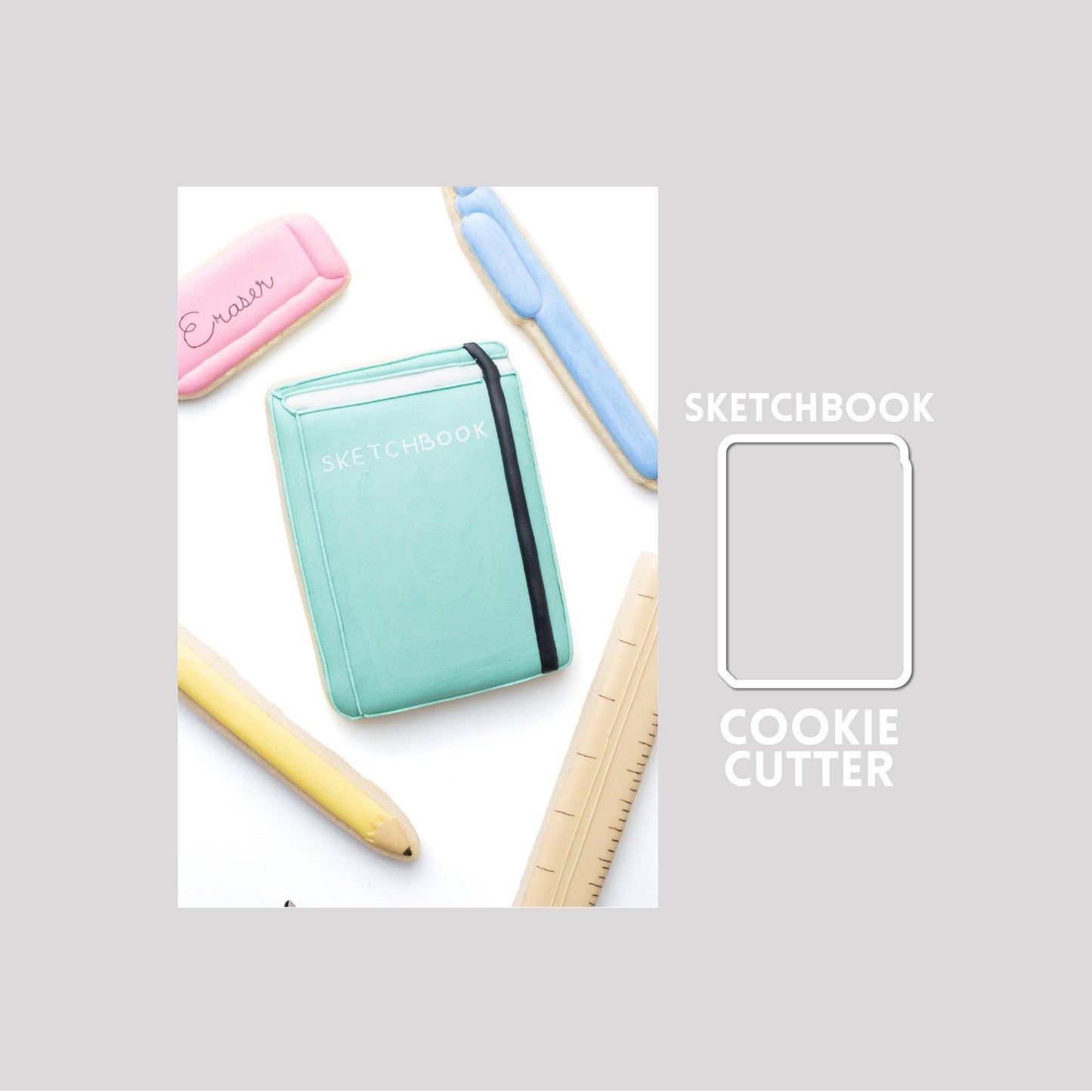 Decorated sketchbook sugar cookie next to a sketchbook cookie cutter outline on a gray background.