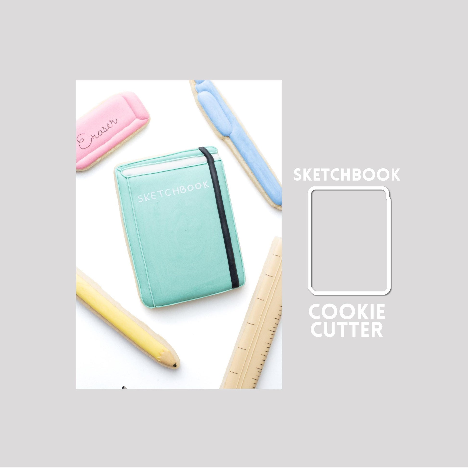 Decorated sketchbook sugar cookie next to a sketchbook cookie cutter outline on a gray background.