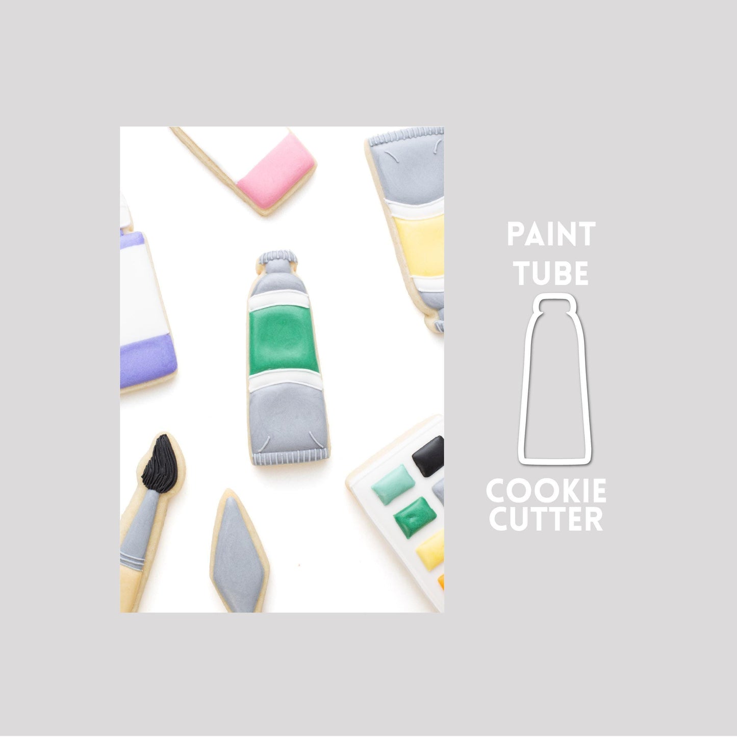 Decorated paint tube sugar cookie next to a paint tube cookie cutter outline on a gray background.