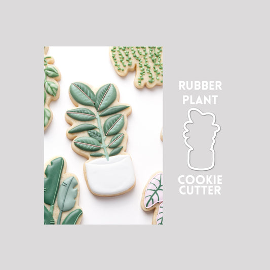 Decorated rubber plant sugar cookie next to a rubber plant cookie cutter outline on a gray background.