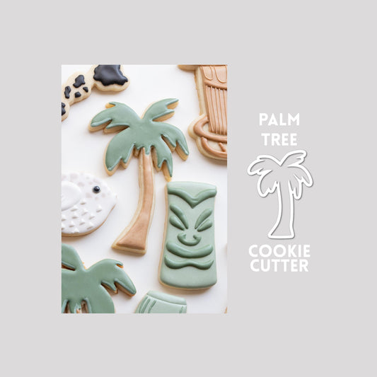 Decorated palm tree sugar cookie next to a palm tree cookie cutter outline on a gray background.