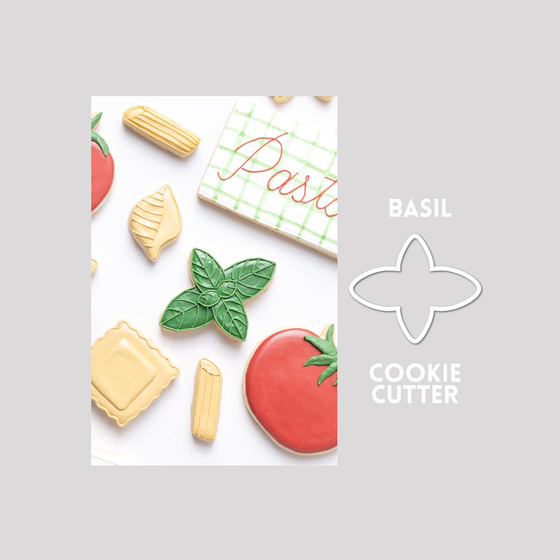 Decorated basil sugar cookie next to a basil cookie cutter outline on a gray background.