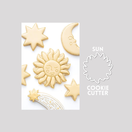 Decorated sun sugar cookie next to a sun cookie cutter outline on a gray background.