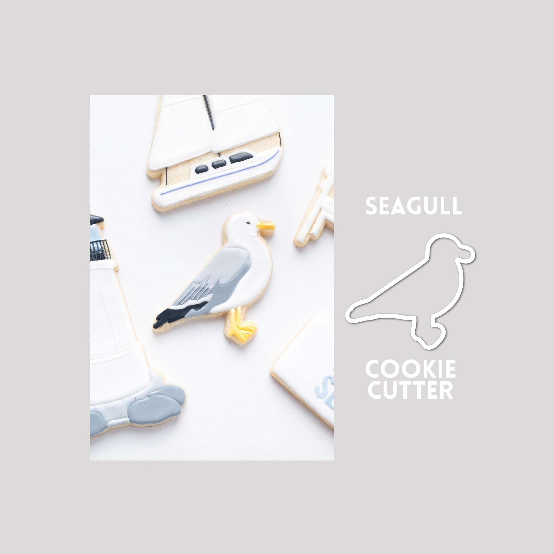 Decorated seagull sugar cookie next to a seagull cookie cutter outline on a gray background.