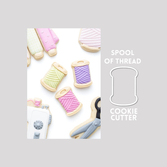 Decorated spool of thread sugar cookie next to a spool of thread cookie cutter outline on a gray background.