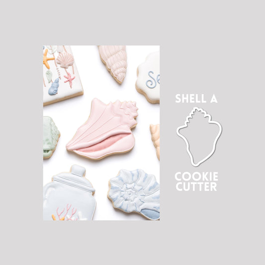 Decorated seashell sugar cookie next to a seashell cookie cutter outline on a gray background.
