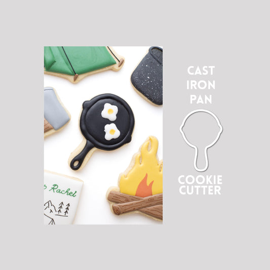 Decorated cast iron pan sugar cookie next to a cast iron pan cookie cutter outline on a gray background.
