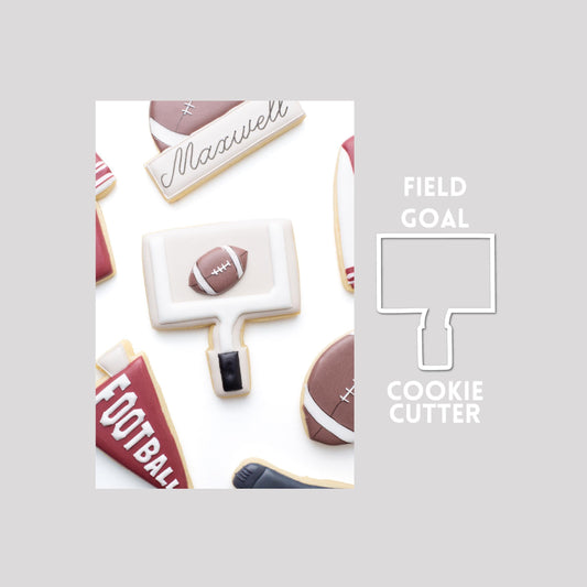 Decorated field goal sugar cookie next to a field goal cookie cutter outline on a gray background.