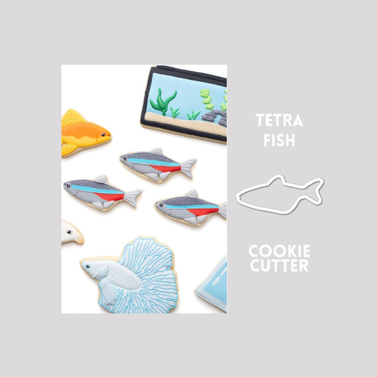 Decorated tetra fish sugar cookie next to a tetra fish cookie cutter outline on a gray background.