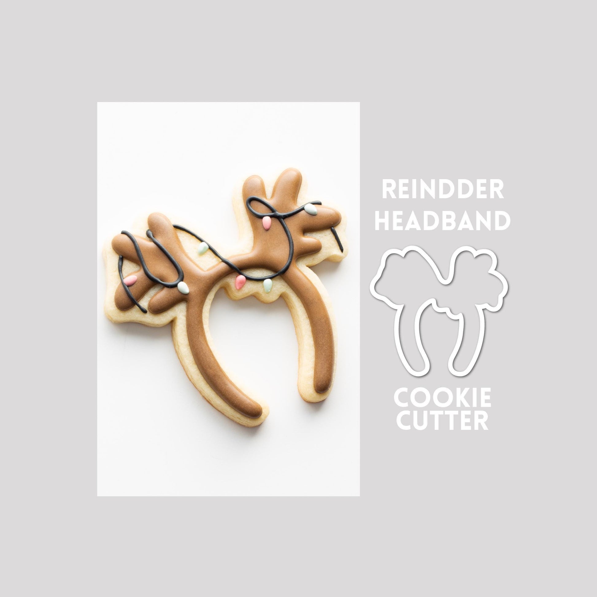 Decorated reindeer headband sugar cookie next to a reindeer headband cookie cutter outline on a gray background.