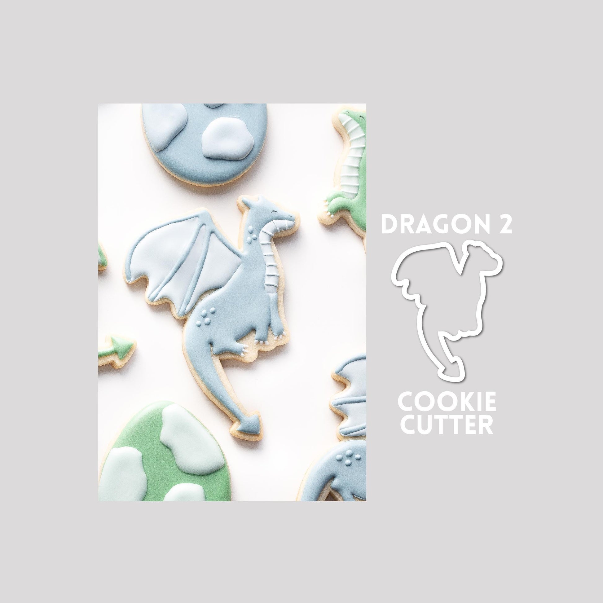 Decorated dragon sugar cookie next to a dragon cookie cutter outline on a gray background.