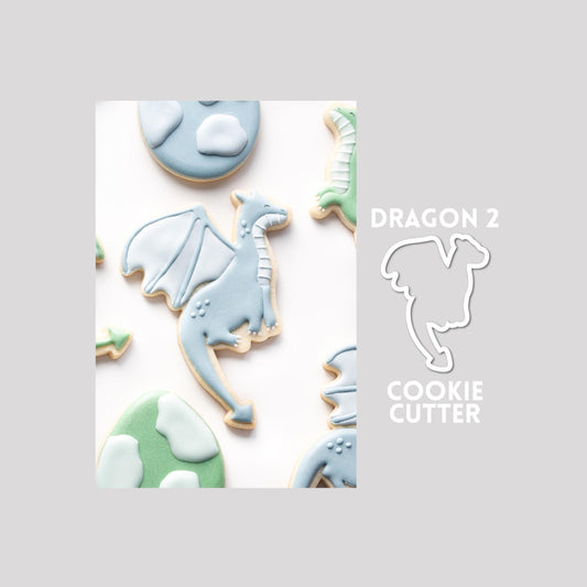 Decorated dragon sugar cookie next to a dragon cookie cutter outline on a gray background.
