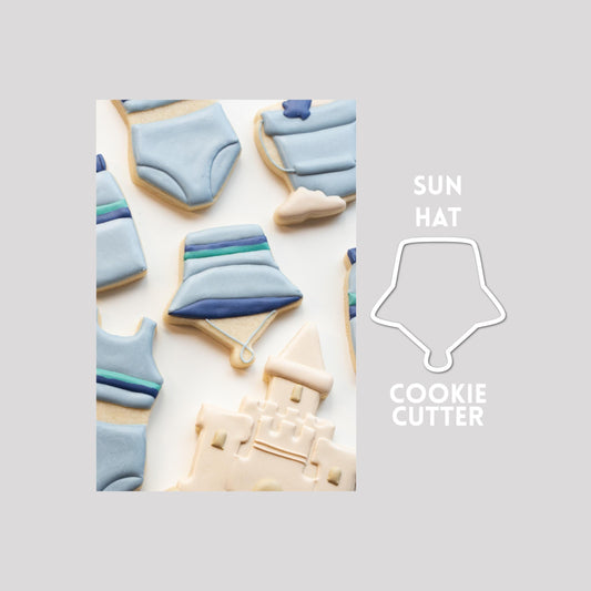 Decorated bucket hat sugar cookie next to a bucket hat cookie cutter outline on a gray background.