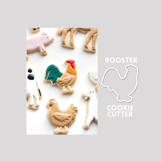 Decorated rooster sugar cookie next to a rooster cookie cutter outline on a gray background.
