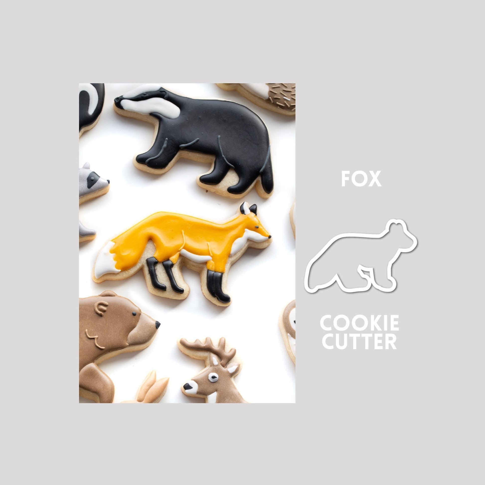 Decorated fox sugar cookie next to a fox cookie cutter outline on a gray background.