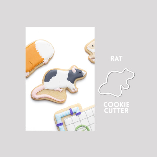 Decorated rat sugar cookie next to a rat cookie cutter outline on a gray background.