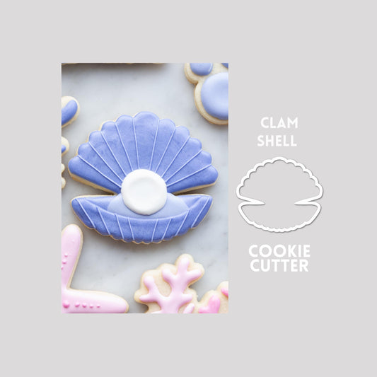 Decorated clam shell sugar cookie next to a clam shell cookie cutter outline on a gray background.