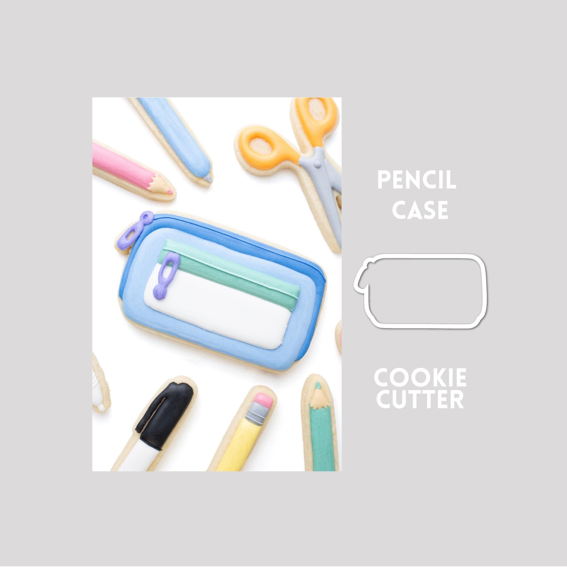 Decorated pencil case sugar cookie next to a pencil case cookie cutter outline on a gray background.