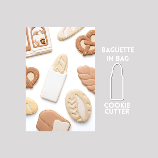 Decorated baguette in bag sugar cookie next to a baguette in bag cookie cutter outline on a gray background.