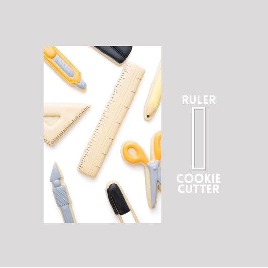 Decorated ruler sugar cookie next to a ruler cookie cutter outline on a gray background.