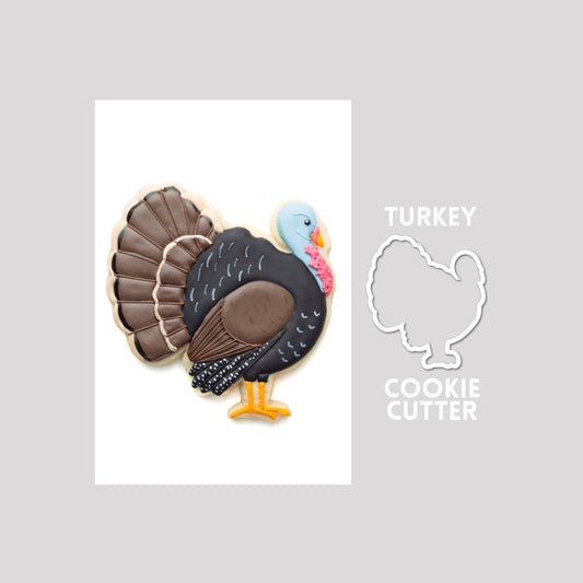 Decorated wild turkey sugar cookie next to a wild turkey cookie cutter outline on a gray background.